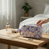Hand holding a light purple floral cosmetics pouch on a table with measurements 15x25cm, next to a bottle of perfume and jewelry