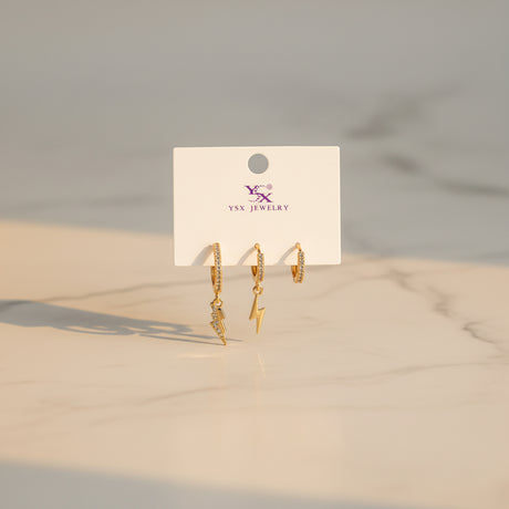Gold lightning earrings on a Jewelry card against a neutral background