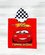 A red hooded towel featuring Lightning McQueen from Disney's Cars, with a black-and-white checkered hood, yellow '95' flame graphic, and yellow 'Lightning McQueen' text, shown on a light wood background