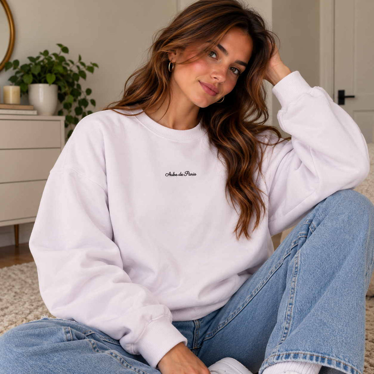 Woman in a lilac crew neck sweatshirt with a dainty Aube de Paris script, hands in her jeans pockets
