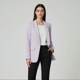 Woman wearing a lilac blazer over a white top and black pants on a plain background