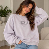 Woman in a lilac crew neck sweatshirt with minimalist Fiore lettering, worn with light jeans