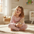 Girl in a lilac pointelle pyjama set sitting on a rug with a teddy