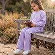 Girl reading on a garden bench in a lilac sweatshirt and flared sweatpants with heart balloon motif