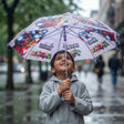Smiling boy in a grey raincoat under a lilac Marvel Heroes umbrella on a rainy street
