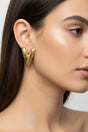 Close-up of a woman wearing gold long heart earrings with a neutral background