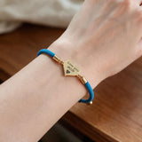 Blue cord bracelet with a gold Love you MOM heart charm on a wrist resting on a table