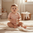 Baby seated on a cream knit blanket in a blush pink bodysuit with a white heart and love you more script