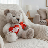 Taupe teddy bear in a red satin bow holding a padded red heart, with a 50cm line