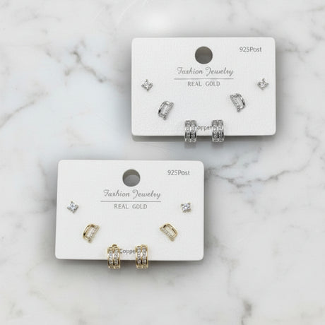 Set of gold and silver luxe earrings on display cards against a marble background