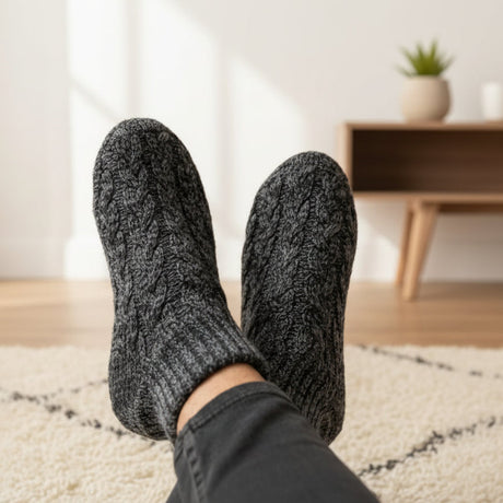 Person wearing dark grey cable knit pantouffle in a home setting with a blurred background
