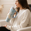 Blue teal marble tumbler with gold veining held in a cream knit sleeve