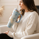 Blue teal marble tumbler with gold veining held in a cream knit sleeve
