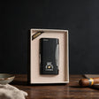 Slim matte black cigar lighter with a printed emblem in a cream gift box next to a cigar