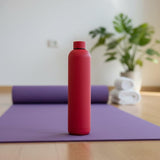 Bright red matte 1L water flask standing on a purple yoga mat