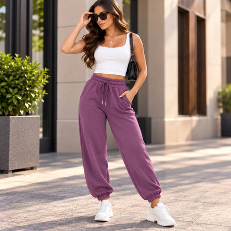 Woman in mauve purple cuffed joggers with a drawstring waist, a white tank crop top and white sneakers