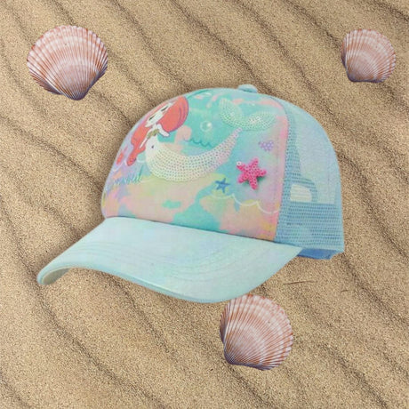 Mint kids cap with a mermaid print, sequin tail and pink starfish patch resting on sand
