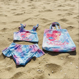 Mermaid-themed children's swimsuit set with matching tote bag on a dark background