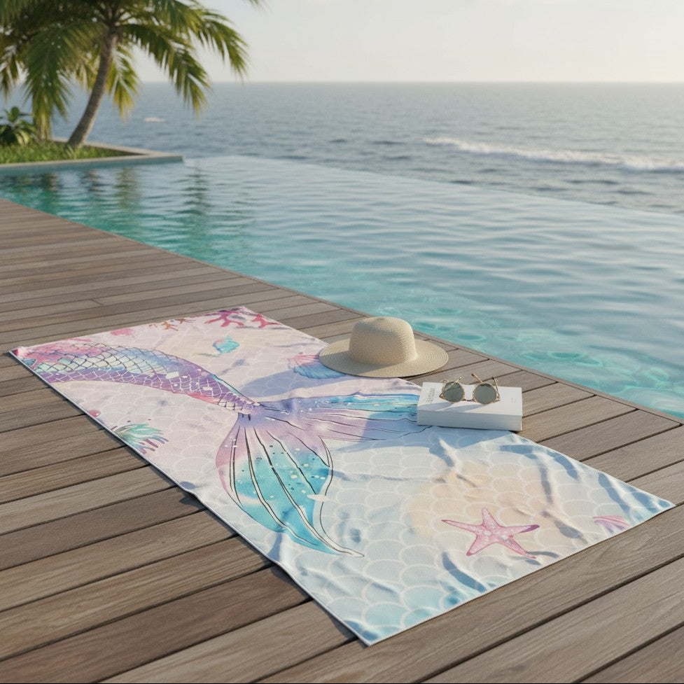 Towel with mermaid design on a wooden deck by a pool with ocean view