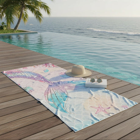 Towel with mermaid design on a wooden deck by a pool with ocean view