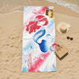 Colorful mermaid-themed beach towel on sand with a hat and bag.