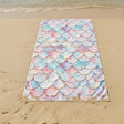 Beach towel with mermaid scale pattern on a sandy beach