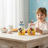 Girl at a breakfast table holding a character glass mug filled with orange juice