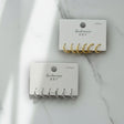 Two sets of gold and silver earring hooks on branded cards against a marble background