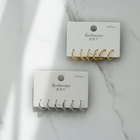 Two sets of gold and silver earring hooks on branded cards against a marble background