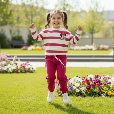 Girl jumping outdoors in a striped Minnie Mouse top and pink jogger set, full length view