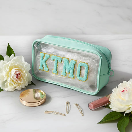 Mint pouch with 'KTMO' text on a white surface with flowers and makeup items