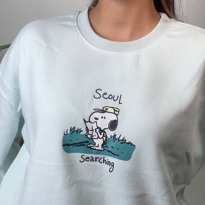 Close up of the puppy scout graphic on a teal grass patch on a mint sweatshirt