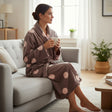 Mocha dressing gown with big blush spots, worn curled up on a grey couch