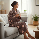 Mocha dressing gown with big blush spots, worn curled up on a grey couch