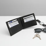 Black wallet with cards, keys, sunglasses, and watch on a white surface