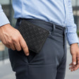 Person holding a black embossed wallet in front of a light blue shirt