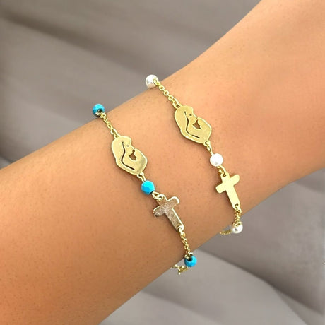 Gold bracelet with Mother Mary symbol on a wrist against a neutral background