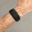 Black leather wrap bracelet on a wrist against a grey background