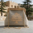 Natural linen clutch with a cedar tree, wooden frame and gold chain in front of an old castle and cedar trees