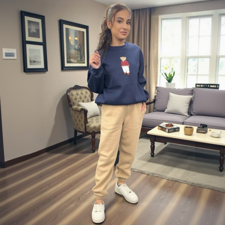 Person wearing a navy sweatshirt with a teddy bear design, and beige sweatpants in a living room