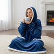 Person wearing a blue hooded blanket holding a mug in a cozy room with a fireplace.