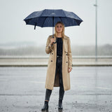 Woman holding a navy blue umbrella in the rain wearing a beige trench coat