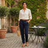 Woman in a white shirt and navy pants standing outdoors with plants and a table in the background