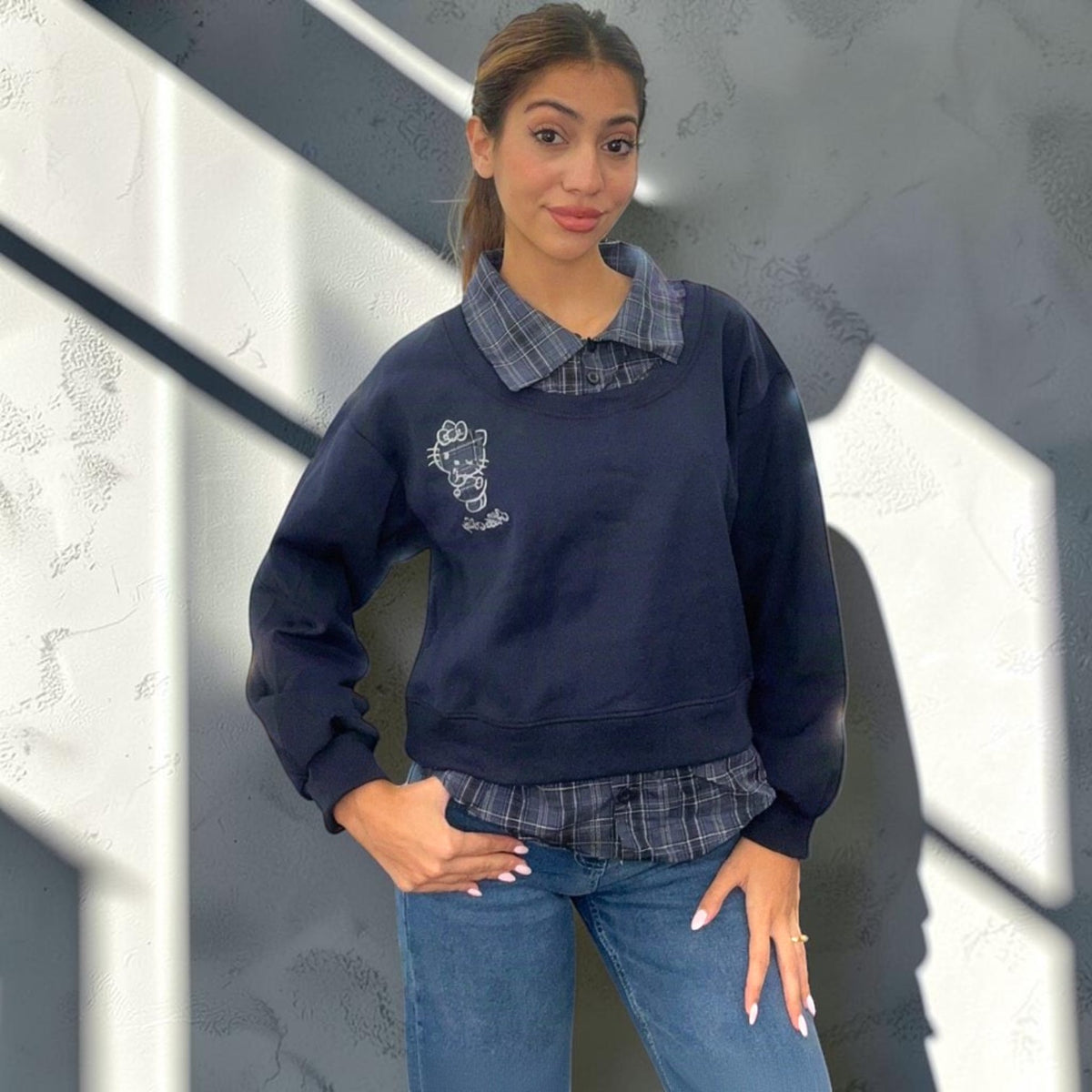Cropped navy sweatshirt layered over a check shirt, styled with straight leg denim
