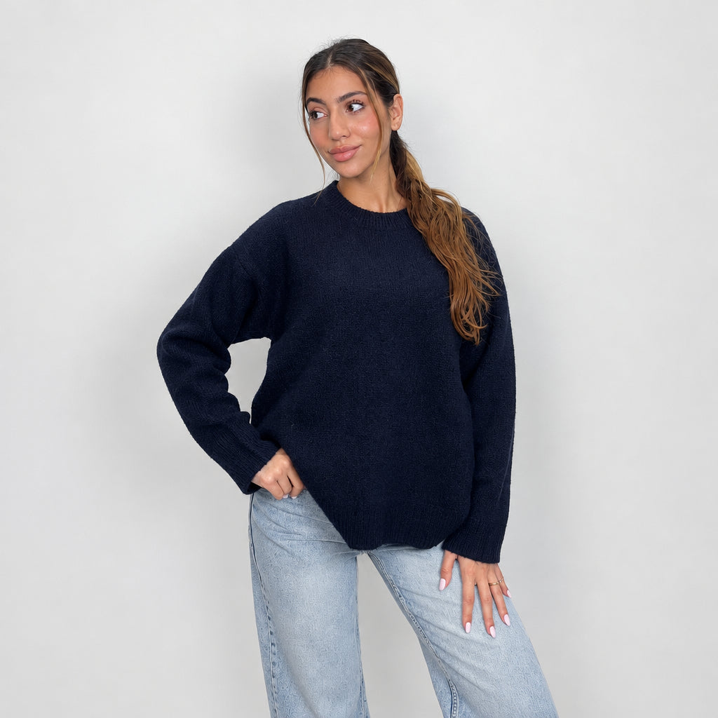 Close view of a dark navy knit sweater with ribbed cuffs, hand on hip