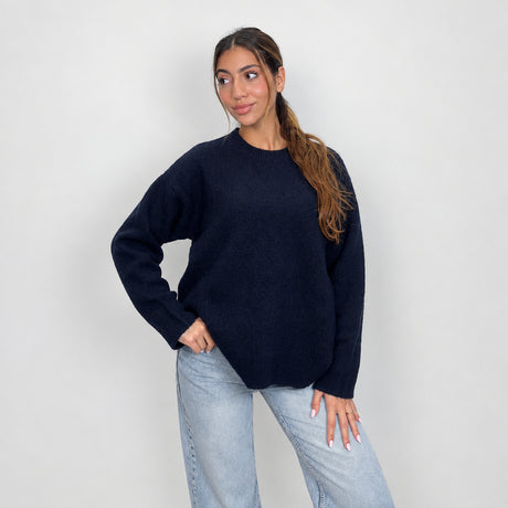 Close view of a dark navy knit sweater with ribbed cuffs, hand on hip