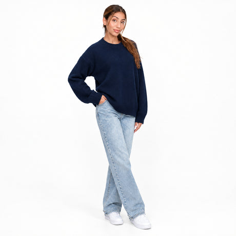Navy crew neck knit sweater worn with straight leg jeans, mid stride