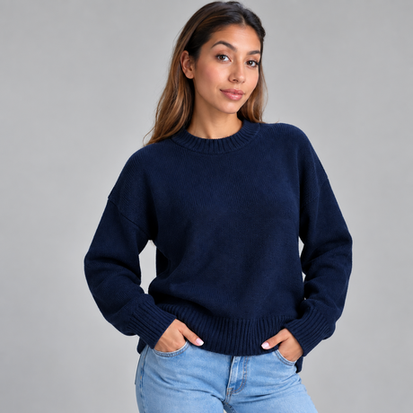 Woman in a navy blue chunky wool knit sweater and light jeans standing with both hands in her pockets
