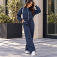 Woman in a navy cropped zip jacket and matching wide leg jogging pants with a white shoulder bag outside a stone building