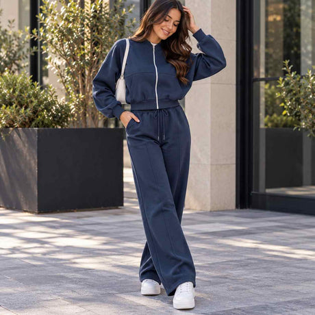 Woman in a navy cropped zip jacket and matching wide leg jogging pants with a white shoulder bag outside a stone building